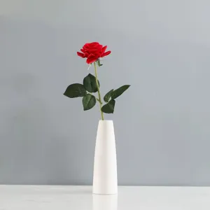 Rose rouge artificielle unique avec des feuilles réalistes dans un vase en céramique blanc