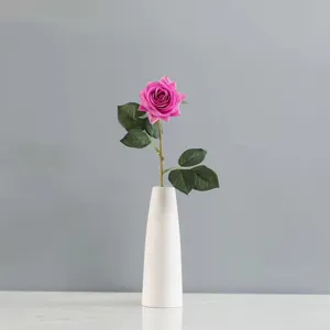 Vue détaillée d'une rose artificielle rose réaliste dans un vase en céramique blanc.