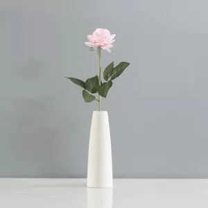 Détail d'une rose artificielle rose au toucher naturel placée dans un vase blanc minimaliste