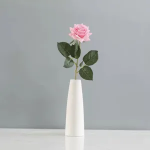 Vue détaillée d'une rose rose artificielle dans un vase blanc minimaliste