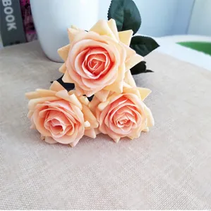 Gros plan de trois roses artificielles champagne sur une texture de jute rustique.