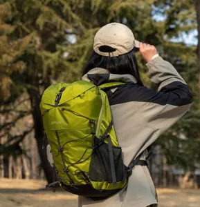 Back view of a person wearing a durable green hiking backpack in an outdoor forest.