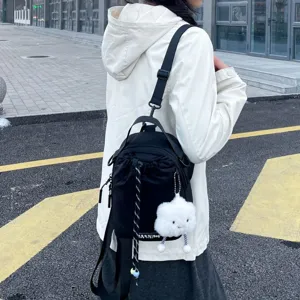 Detail view of a black mini backpack with drawstring closure and cute white cloud plush pendant outdoors.
