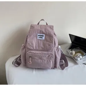 Dettaglio zaino casual in tela viola con tasca frontale con zip ed etichetta elegante.