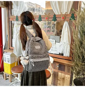 Chica con mochila gris estilo preppy con encaje y patrones de corazones en un café.