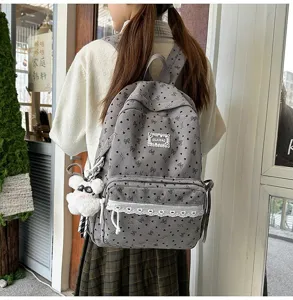 Detalle de mochila de pana gris con corazones, encaje blanco y colgante de osito de peluche.