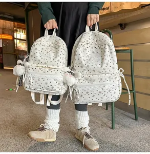 Vista detallada de mochilas blancas estilo académico con patrones de corazones y encaje