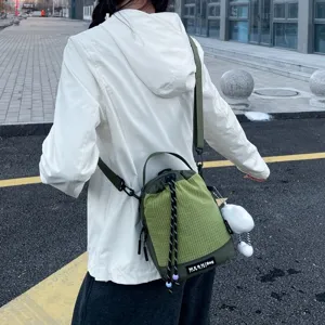 Detail view of green grid crossbody water cup bag with drawstring and plush pendant outdoor.