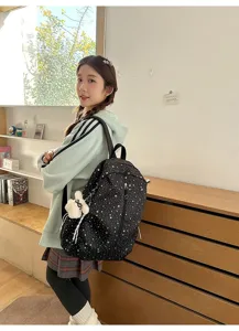 Vista trasera de una mochila negra para estudiante con diseño de estrellas y colgante.
