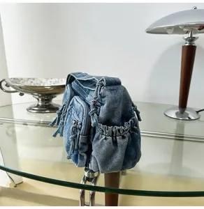 Denim schoudertas detail met meerdere zakken, ritsen en gewassen textuur op glazen tafel geplaatst.