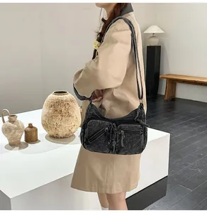 Gewassen denim crossbody tas detailopname met meerdere zakken en verstelbare schouderriem.