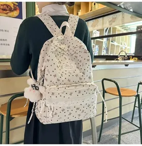 Detalle de mochila de pana crema con estampados de lazos marrones y un colgante suave