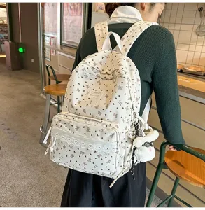Detalle de una mochila de pana blanca con estampados de corazones y colgante de conejo.