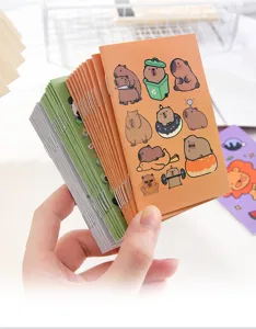 Detailed view of a stack of cute cartoon capybara mini notebooks held in hand for scale