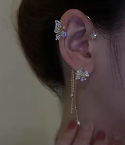 Detalle de un ear cuff de mariposa con circonitas y borlas largas doradas en modelo.