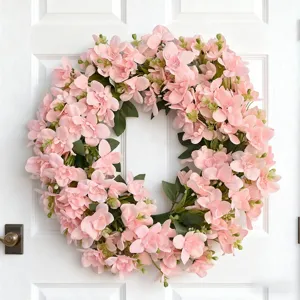 Corona de flores rosas colgando de puerta de madera blanca para decoración del hogar.