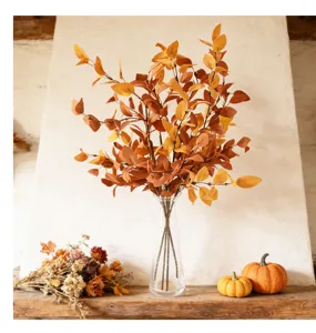 Artificial autumn eucalyptus branch in clear glass vase, rustic tabletop fall decor.