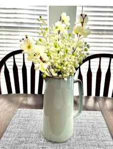 Detailed view of white artificial flowers and green berries arranged in a green ceramic pitcher