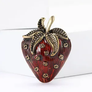 Detailed view of a vintage red enamel strawberry brooch with gold-toned metal leaves.