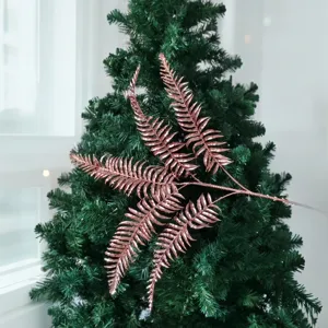 Détail de branche de feuille persane à paillettes or rose sur un sapin de Noël vert.