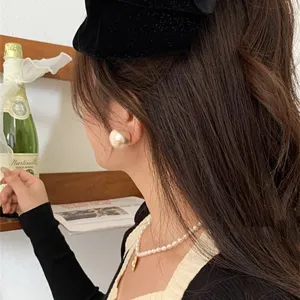 Detailed side view of an oversized retro champagne gold pearl stud earring worn by a model