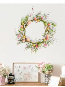 Handcrafted Easter wreath decorated with pastel eggs and pink berries on a white wall