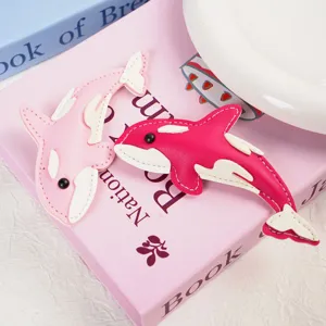 Detail shot of light pink and magenta leather orca-shaped keychains on a book background.