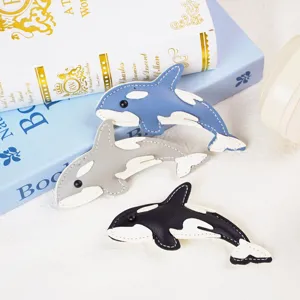 Detail view of handmade leather orca charms in blue, grey, and black with white stitching.