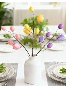 Close-up of decorative Easter egg and tulip floral branch arranged in a white ceramic vase