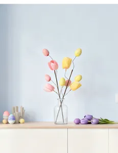 Detailed view of Easter tulip and egg branch decoration in a glass vase on a table.