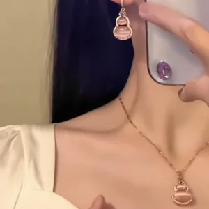 Detail view of pink cat eye stone gourd pendant necklace and earrings set on a model