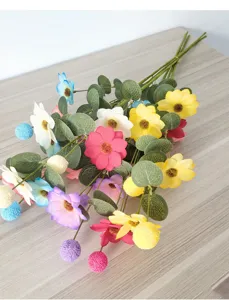 Nahaufnahme von bunten künstlichen Gänseblümchen mit Eukalyptusblättern auf Holz