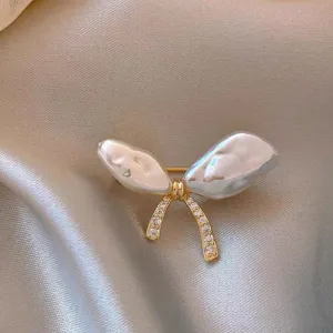Macro detail of irregular iridescent pearl bow brooch with crystal-encrusted gold ribbon.