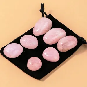 Seven polished natural rose quartz stones with black velvet pouch on peach background