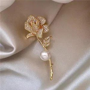 Elegant gold rose flower brooch featuring sparkling crystals and a large pearl detail