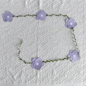 Purple paper flower garland with green leaves on white textured fabric background