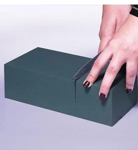 Detailansicht eines grünen Steckmoosblocks beim Schneiden, ideal für Blumenarrangements.