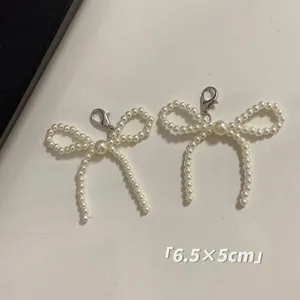 Detail view of two elegant pearl bow charms with silver lobster clasps, 6.5x5cm.