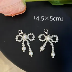 Detail shot of pearl bow shoe charms with silver lobster clasp on black background.