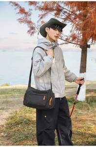 Outdoor-Lifestyle-Foto einer großen schwarzen karierten Kuriertasche mit orangem Reißverschluss.