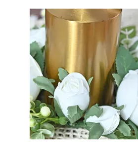Close-up detail of white silk roses and a gold brushed metal candle holder base.