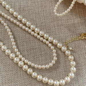 Detailaufnahme einer eleganten weißen Perlenkette mit goldenem Verschluss auf Leinenstoff