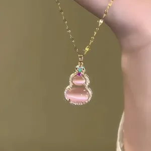 Detailed view of a pink cat's eye stone gourd pendant on a gold-toned necklace.