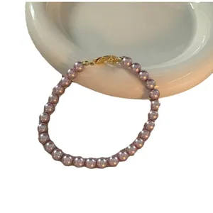 Elegante minimalistische lila-rosa Perlenkette mit verstellbarem Goldverschluss auf weißem Teller