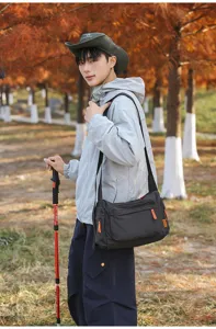 Mann trägt eine große karierte Kuriertasche in einer herbstlichen Außenumgebung.