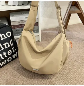 Minimalist beige crescent dumpling bag with wide shoulder strap and orange zipper detail.