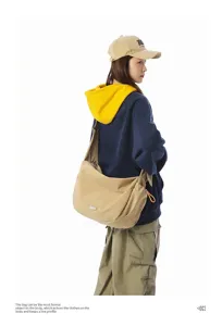 Large khaki messenger bag with dumpling shape worn by model over a navy hoodie