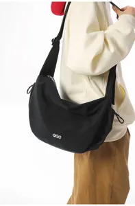 Detail of a black crescent-shaped messenger bag worn by a model in a white hoodie.