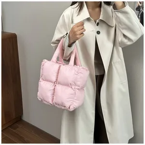 Detail of a stylish pink quilted puffer tote bag carried by a model in a white coat.