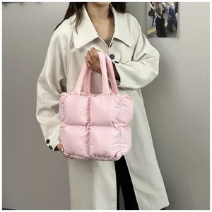 Detail view of a soft pink padded quilted tote bag held by a woman in a cream coat